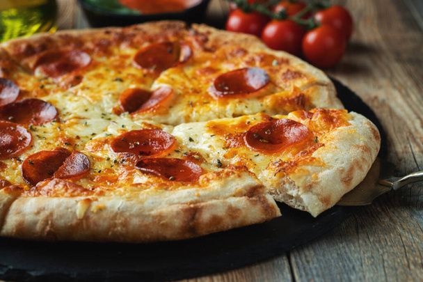 チーズを伸ばしたホットイタリアのピザのスライス. 暗い木の背景にピザペッパーニ. - 写真・画像