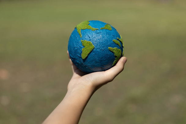 Young boys hand holding planet Earth globe at natural park background as Earth day to save this planet with ESG principle and environment friendly energy for brighter future. Gyre - Photo, Image