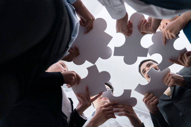 Below view of diverse corporate officer workers collaborate in office connecting puzzle pieces as partnership and teamwork concept. Unity and synergy in business idea by merging jigsaw puzzle. Concord - Photo, Image