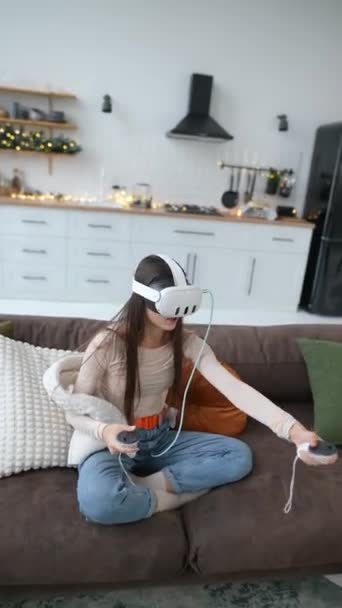 Egy bájos fiatal nő kommunikál egy virtuális valóság fülhallgatón keresztül, egy karácsonyfának támasztva. Kiváló minőségű 4k felvételek - Felvétel, videó