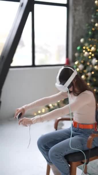 Avec un arbre de Noël en arrière-plan, une jeune femme élégante utilise un casque de réalité virtuelle. Images 4k de haute qualité - Séquence, vidéo