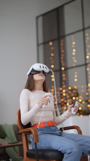 Una hermosa joven jugando a un juego con un auricular de realidad virtual en una casa decorada con Navidad. Imágenes de alta calidad 4k - Metraje, vídeo