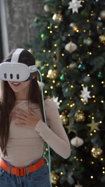 Egy fiatal nő virtuális valóság szemüvegben egy karácsonyi díszítésű otthonban. Kiváló minőségű 4k felvételek - Felvétel, videó