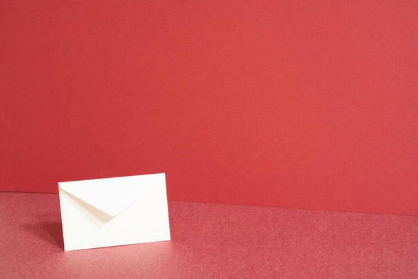 Sobre de papel blanco sobre mesa roja. fondo de pared roja - Foto, Imagen