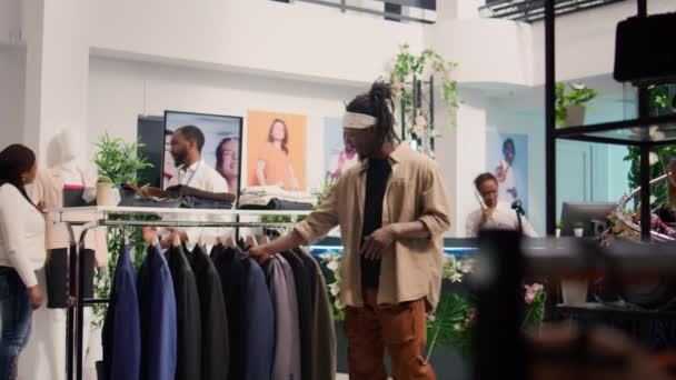 Πελάτης που φτάνει στο κατάστημα ρούχων κατά τη διάρκεια της διαφημιστικής περιόδου, ψάχνει να αγοράσει φθηνά ρούχα για να γεμίσει την ντουλάπα του. Ο άνθρωπος που εκμεταλλεύεται τις πωλήσεις στην μπουτίκ μόδας, κοιτάζοντας κομψά μπλέιζερ - Πλάνα, βίντεο