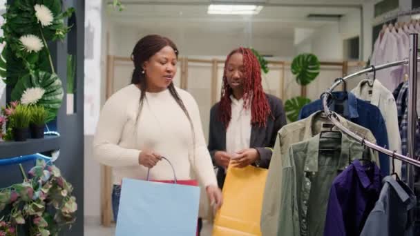 Ευτυχισμένοι φίλοι στο κατάστημα ρούχων κατά τη διάρκεια της διαφημιστικής περιόδου, αγοράζοντας φθηνά ρούχα. Οι πελάτες ενθουσιασμένοι για τις πωλήσεις στην μπουτίκ μόδας, γεμίζοντας τσάντες αγορών με πολλά ρούχα - Πλάνα, βίντεο