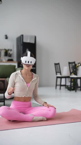 Eine sportliche junge Frau vertieft sich während der Festtage zu Hause in Yoga, unterstützt von einem Virtual-Reality-Headset. Hochwertiges 4k Filmmaterial - Filmmaterial, Video