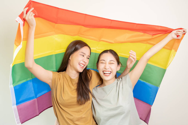LGBTグループ。良い探してレズビアンのカップルが明るく虹のフラグをカバー笑顔。アジアの若いカップルは、愛、バイセクシャル、同性愛、自由、表現、幸せな生活の中でお互いに喜んで抱き合っています - 写真・画像