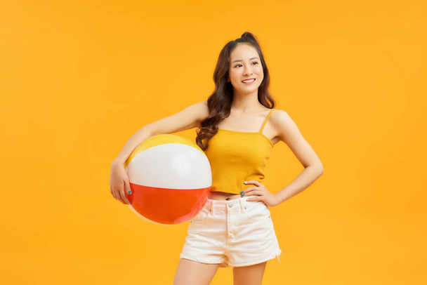 Молодая азиатка держит пляжный мяч изолированы на ярком желтом фоне счастливы  - Фото, изображение