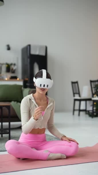 Stylowa młoda kobieta obejmuje jogę w domu w okresie świątecznym, wykorzystując zestaw słuchawkowy wirtualnej rzeczywistości. Wysokiej jakości materiał 4k - Materiał filmowy, wideo