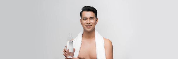 Portret młodego mężczyzny z białym ręcznikiem na ramieniu trzymającego butelkę wody na białym tle - Zdjęcie, obraz