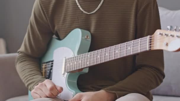 Vystřižený záběr nepoznatelného muže sedícího doma na pohovce a hrajícího na elektrickou kytaru - Záběry, video
