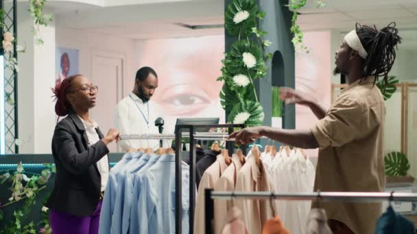Varejista em loja de roupas usando tecnologia de realidade aumentada para mostrar opções de vestuário do cliente para ele escolher. Empregado usando hologramas AR para ajudar o cliente a visualizar o traje necessário - Filmagem, Vídeo