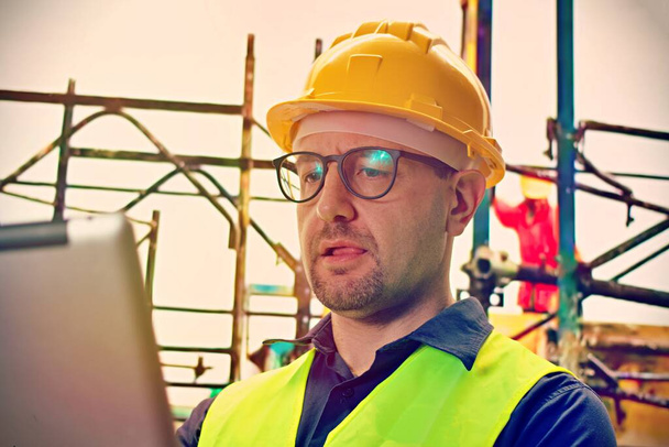 Een portret van een industrieel ingenieur met een bril met laptop op een bouwplaats, werkend. - Foto, afbeelding