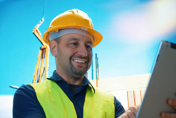 Standing smiling and holding digital tablet. Businessman in working clothes is on the construction site at daytime - Photo, Image