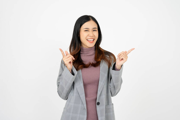 Joven mujer de negocios asiática, sonriendo mientras señala con el dedo, recomendando producto, alabanza, de pie sobre fondo blanco. - Foto, Imagen