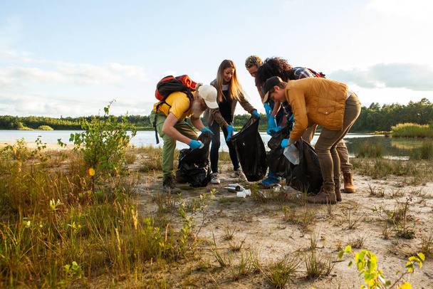 Dieses Bild zeigt eine Gruppe von Personen, die aktiv an den Aufräumarbeiten am See beteiligt sind. In lässiger Outdoor-Kleidung und bewaffnet mit Müllsäcken und Handschuhen beugen sie sich vor und sammeln Müll auf. - Foto, Bild