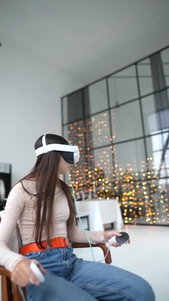 Μέσα σε ένα εορταστικά διακοσμημένο διαμέρισμα της Πρωτοχρονιάς, ένα μοντέρνο κορίτσι δουλεύει με ένα σετ κεφαλής εικονικής πραγματικότητας. Υψηλής ποιότητας 4k πλάνα - Πλάνα, βίντεο
