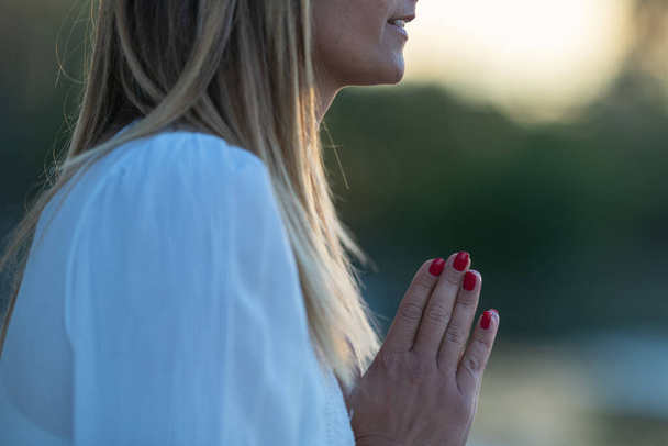 A kezek imádkozó helyzetben találkoznak a víz melletti békés meditáció során, elősegítve a belső nyugalmat és a természettel való kapcsolatot. - Fotó, kép