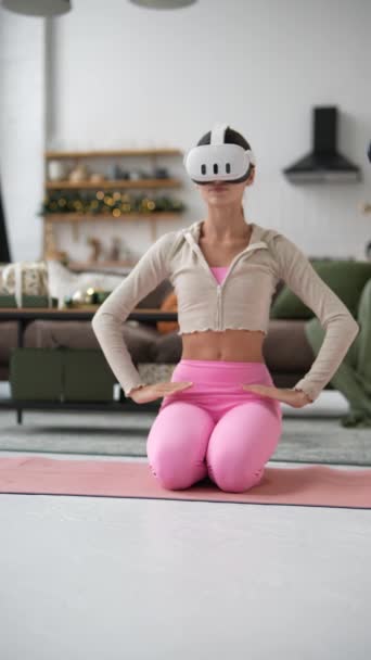 Joulukuusen taustalla kaunis nuori nainen harjoittaa joogaa virtuaalitodellisuuskuulokkeilla. Laadukas 4k kuvamateriaalia - Materiaali, video