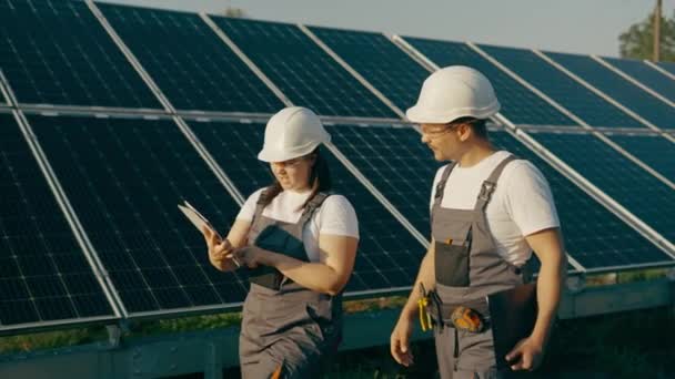Une jeune fille ingénieur et son assistante parcourent des panneaux solaires photovoltaïques et analysent le résultat de l'énergie verte et de l'énergie renouvelable.Concept d'énergie verte dans une centrale solaire. - Séquence, vidéo