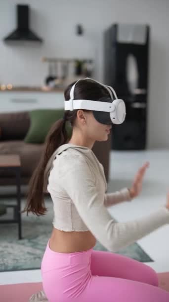 Aktywna młoda kobieta podczas wakacji ćwiczy za pomocą zestawu słuchawkowego wirtualnej rzeczywistości w domu. Wysokiej jakości materiał 4k - Materiał filmowy, wideo