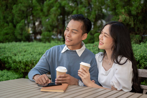 Junges entzückendes asiatisches Paar, das Zeit miteinander im Park verbringt und eng beieinander sitzt. Hängepartie - Foto, Bild