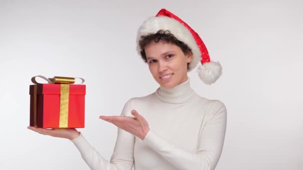 Noel Baba şapkalı mutlu kız elinde beyaz arka planda bir Noel hediyesi tutuyor. Yüksek kalite 4k görüntü - Video, Çekim