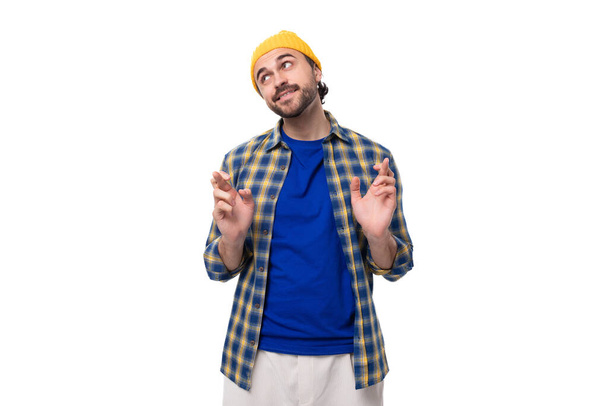 gepflegter, authentischer junger, brünetter Mann mit brutalem Bart und Schnurrbart, bekleidet mit gelbem Hut und blauem Hemd. - Foto, Bild