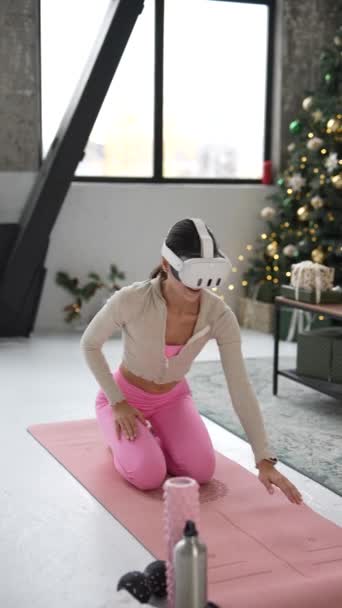 Engagée dans l'exercice à la maison pendant Noël, une jeune femme active utilise un casque de réalité virtuelle. Images 4k de haute qualité - Séquence, vidéo