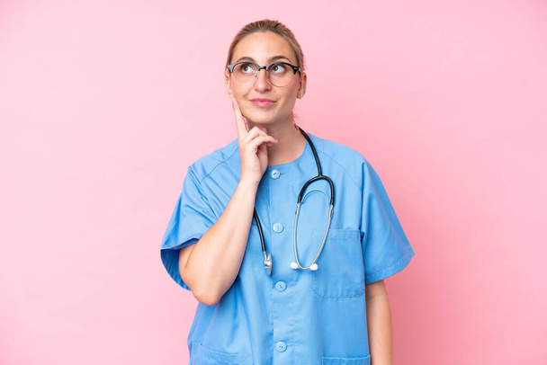 Νεαρή χειρουργός νοσοκόμα γυναίκα απομονωμένη σε ροζ φόντο σκέφτεται μια ιδέα, ενώ ψάχνει επάνω - Φωτογραφία, εικόνα