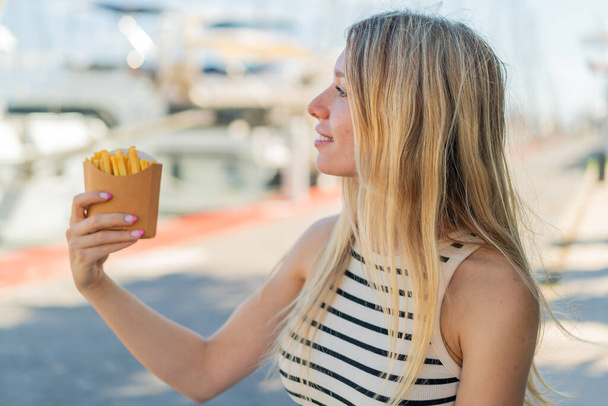 Jeune femme blonde tenant des chips frites à l'extérieur avec une expression heureuse - Photo, image