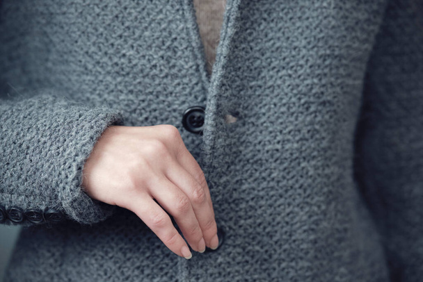 Close-up van een grijs gebreid jasje en een vrouwenhand. Winter, herfst warme wollen kleding. - Foto, afbeelding