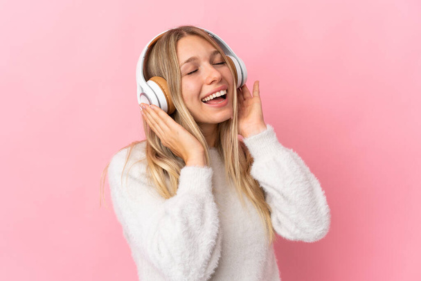 fiatal szőke nő elszigetelt rózsaszín háttér hallgat zenét és énekel - Fotó, kép