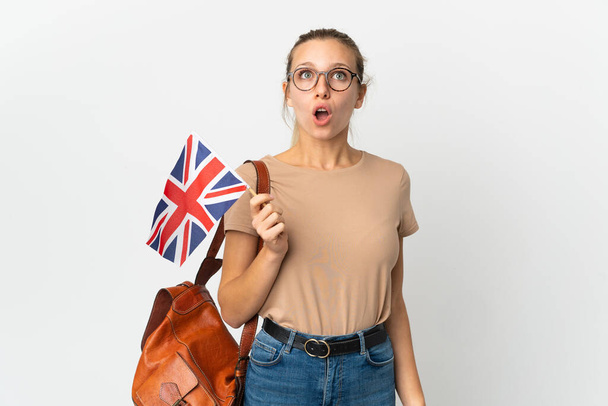 Junge blonde Frau mit einer britischen Flagge auf weißem Hintergrund, die mit überraschtem Gesichtsausdruck nach oben blickt - Foto, Bild