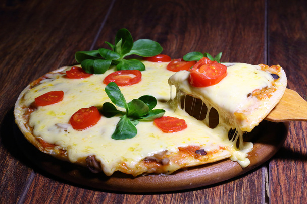 Pedazo de pizza con queso fundido en una pala de madera
 - Foto, imagen