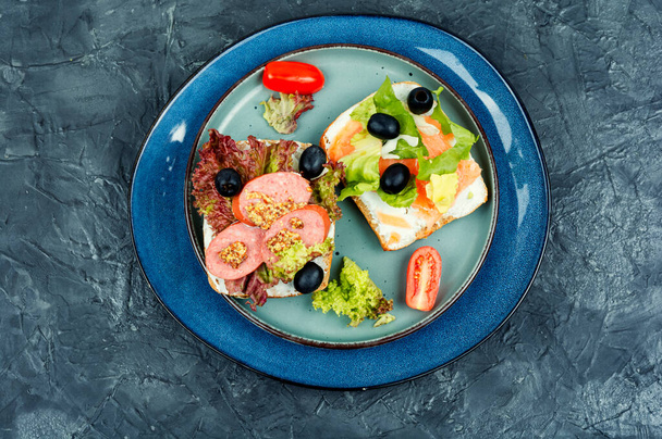Hausgemachte Sandwiches mit gesalzenem roten Fisch und Würstchen. Getreidebrot mit Frischkäse-Fisch und Salami, schwarzen Oliven und Gemüse. Frühstück - Foto, Bild