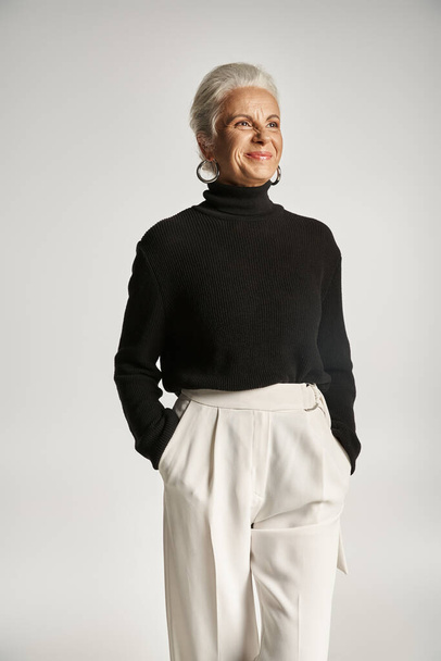 portret van gelukkige middelbare leeftijd zakenvrouw in elegante kleding poseren met de handen in zakken op grijs - Foto, afbeelding