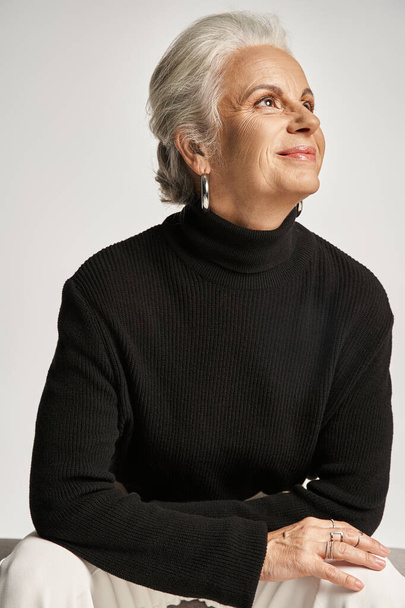 business portrait, happy middle aged business woman in turtleneck looking away on grey backdrop - Photo, Image