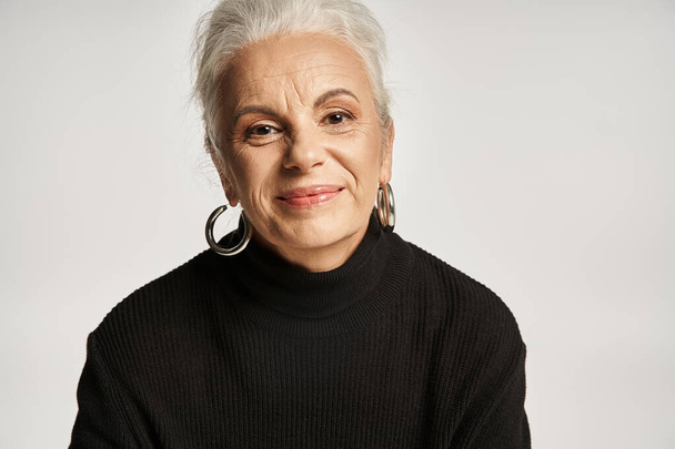 business portrait, happy middle aged business woman in turtleneck looking away on grey backdrop - Photo, Image