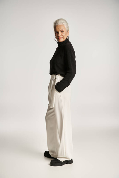 volledige lengte van gelukkig middelbare leeftijd zakenvrouw in elegante kleding poseren met de handen in zakken - Foto, afbeelding
