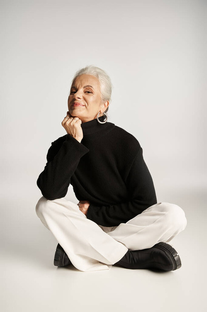 vrolijke middelbare leeftijd zakenvrouw in elegante slimme casual kleding zitten op grijze achtergrond - Foto, afbeelding
