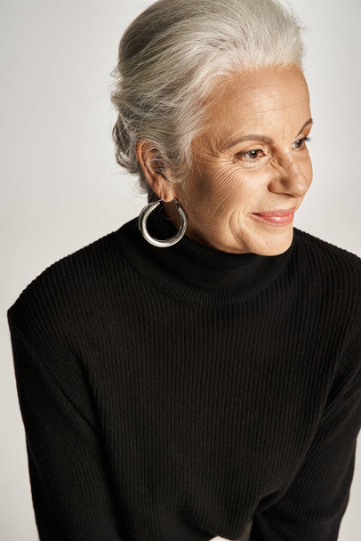 portrét veselé podnikatelky středního věku v elegantním oblečení a obruče náušnice na šedém pozadí - Fotografie, Obrázek