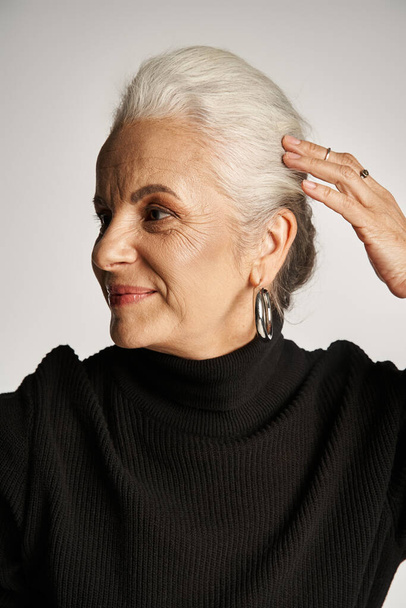retrato de mujer de negocios de mediana edad feliz en traje elegante y aretes de aro ajustando el pelo gris - Foto, Imagen