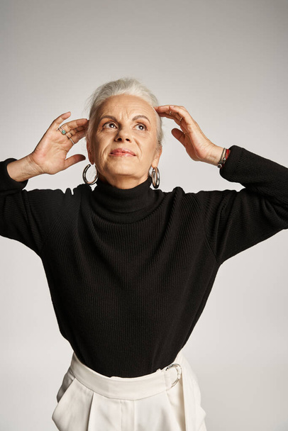 portrait of happy middle aged business woman in elegant attire and hoop earrings adjusting grey hair - Photo, Image