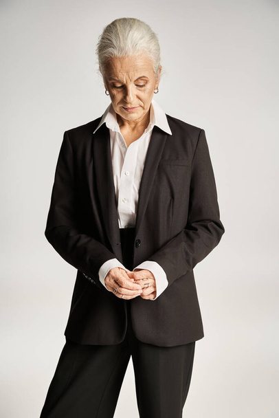 портрет бізнес-леді середнього віку в білій сорочці і штанях, що стоять на сірому фоні - Фото, зображення