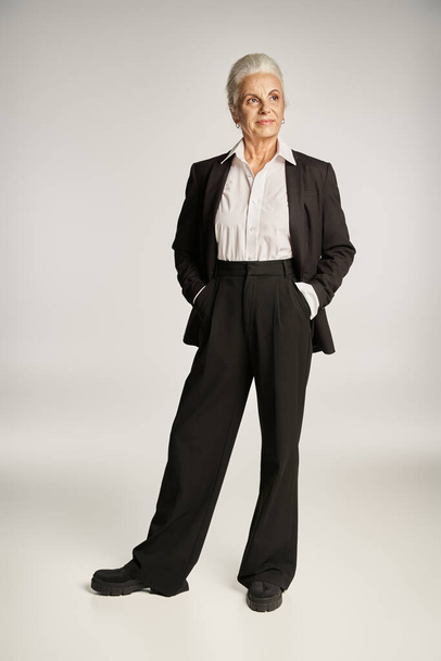 longitud completa de la feliz mujer de negocios de mediana edad en camisa y pantalones de pie con las manos en los bolsillos - Foto, Imagen