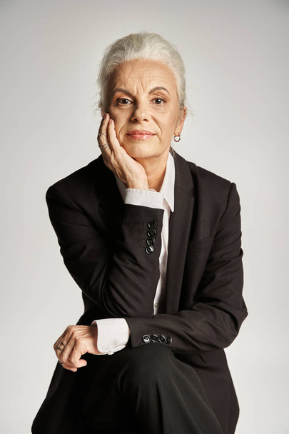 hermosa y gris mujer de mediana edad en traje elegante posando sobre fondo gris - Foto, Imagen