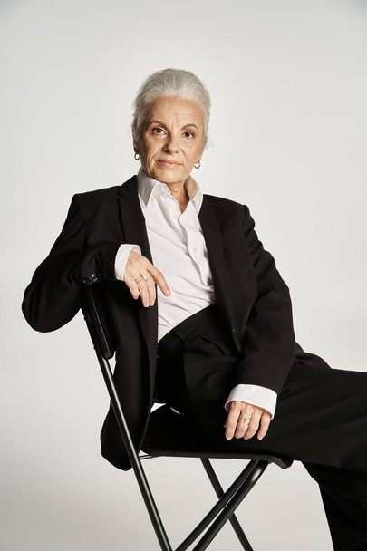 mooie en grijze harige vrouw van middelbare leeftijd in elegante kleding rusten op grijze achtergrond - Foto, afbeelding