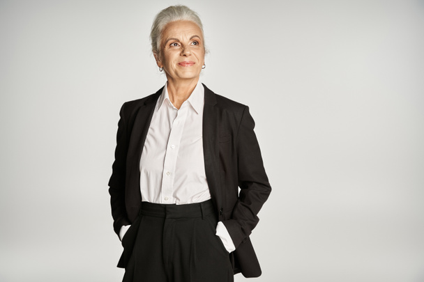 beautiful and grey haired middle aged woman in elegant attire posing on grey background - Photo, Image
